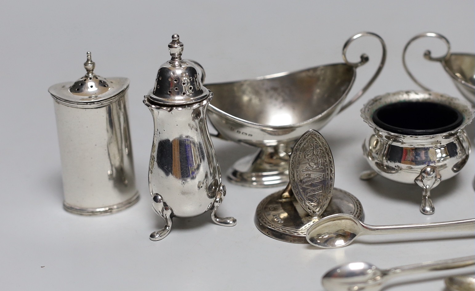 A pair of George V silver two handled boat shaped pedestal salts length 10.7cm, a pair of Edwardian silver pepperettes, a pair of late Victorian silver menu holders, a pair of silver sugar tongs and a three piece plated